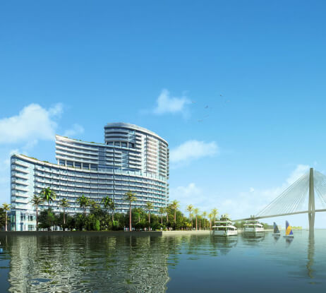 A modern, curved high-rise building stands by the water with palm trees along the shore. Sailboats and yachts are nearby, and a large cable-stayed bridge extends across the scene under a clear blue sky.